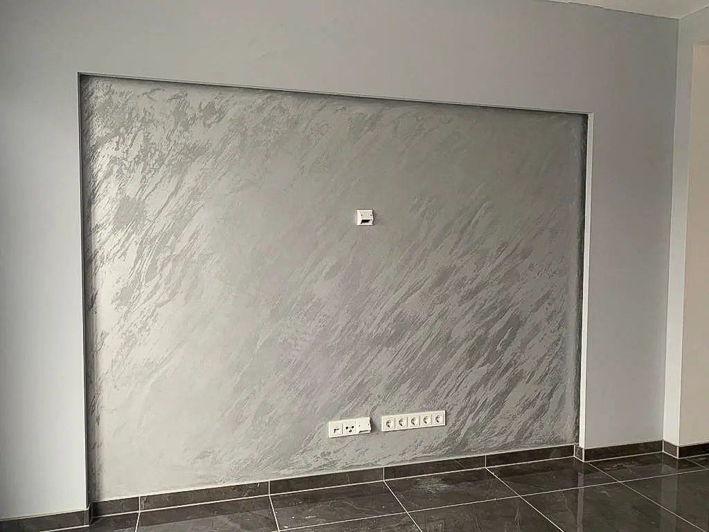 Eine Wandnische mit edler Spachteltechnik in grau-silbernem Farbton, die einen marmorartigen Effekt erzeugt; darunter sind glänzende Bodenfliesen zu sehen.